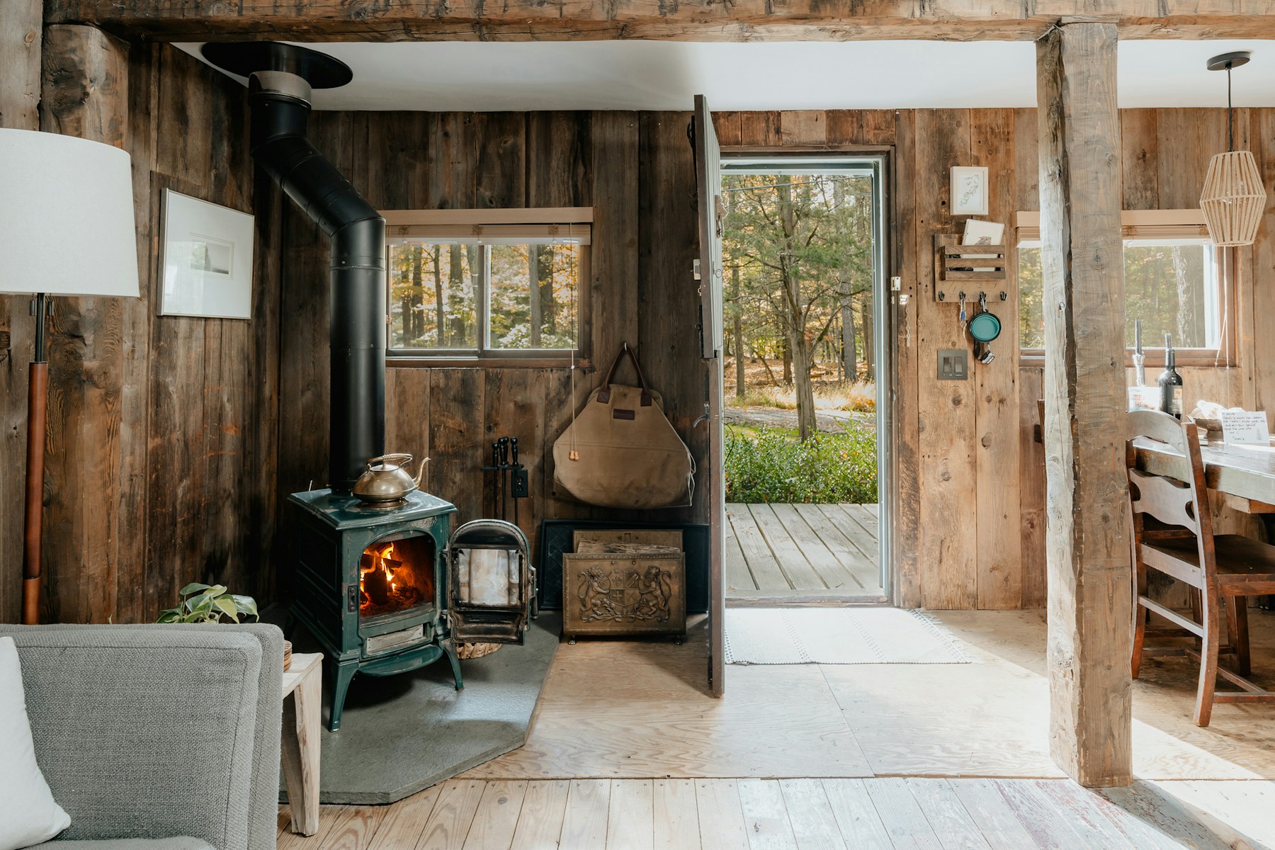 A wooden cabin with a glowing wood stove and an open door to the forest.