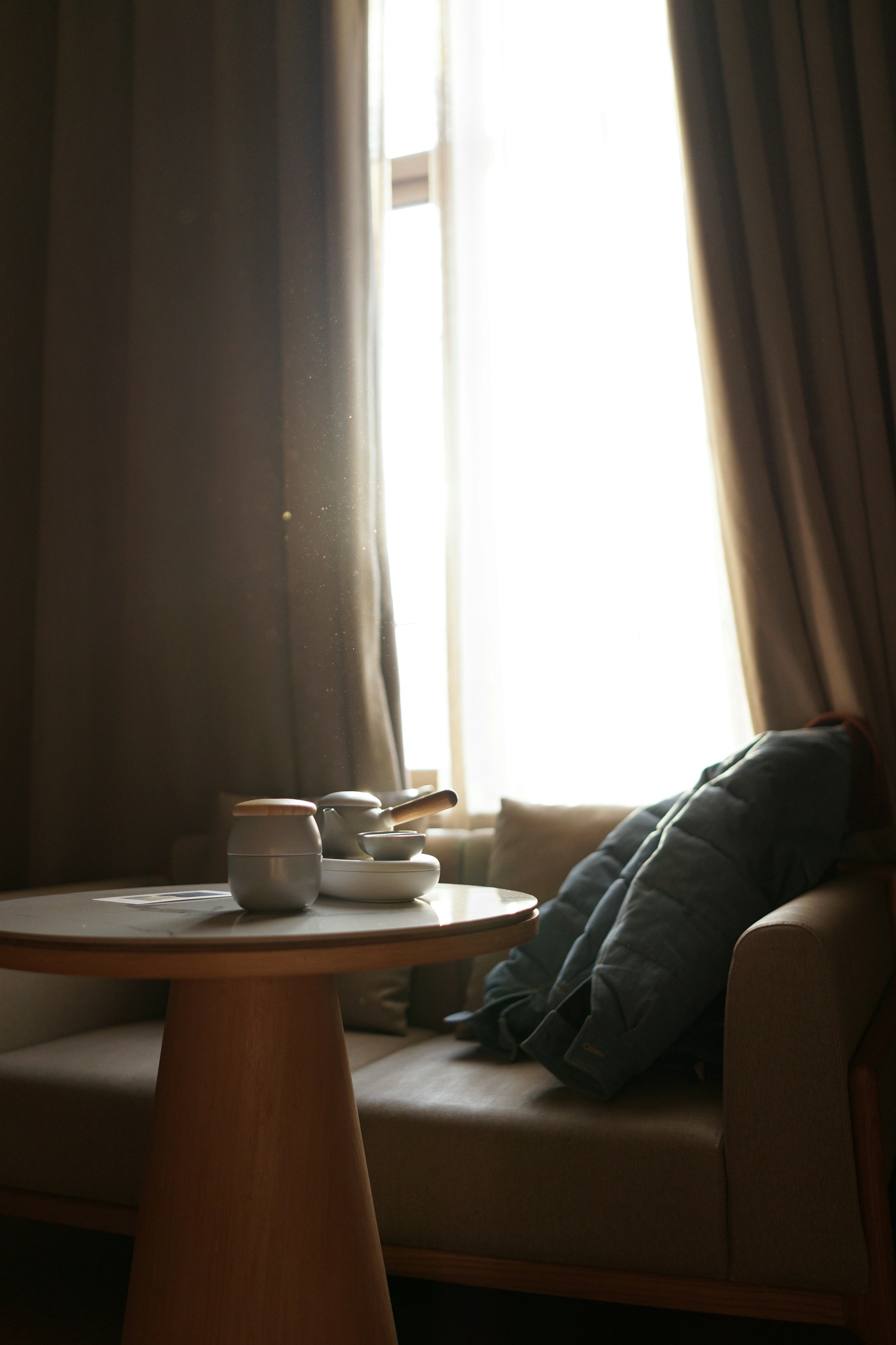 A tea table and cushioned chair beside a softly lit window.
